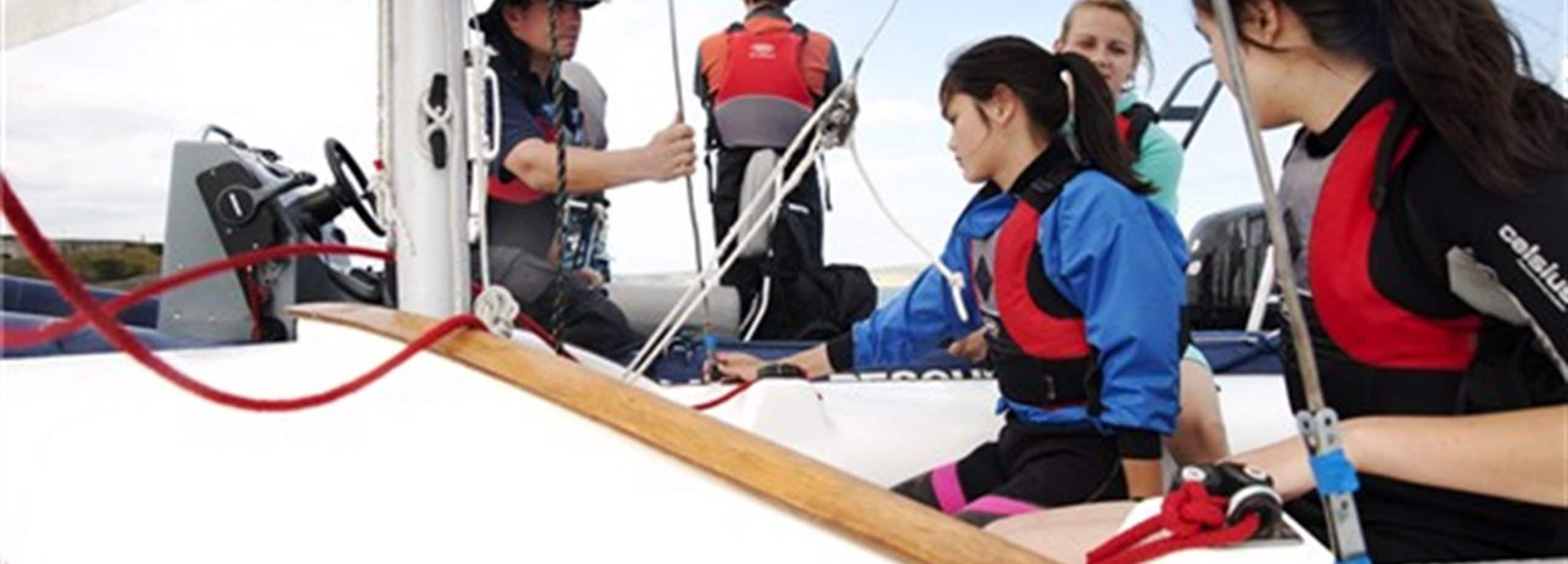 Young people sit in a sailing boat