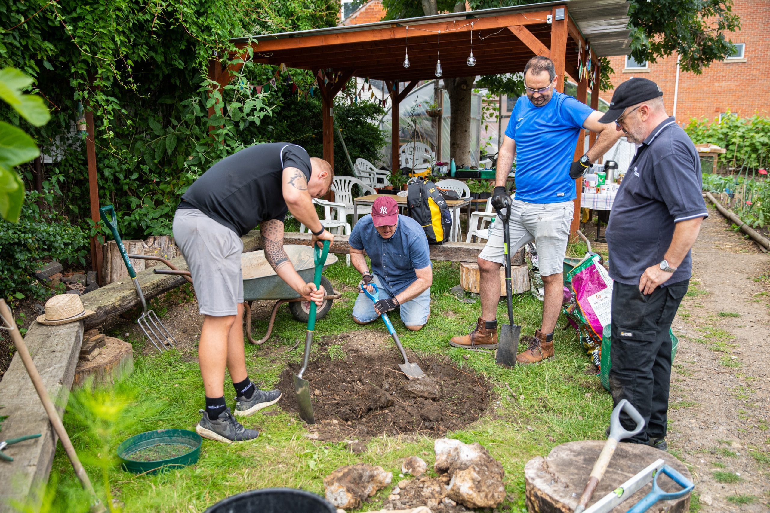 Four men are digging a hole in a lawn