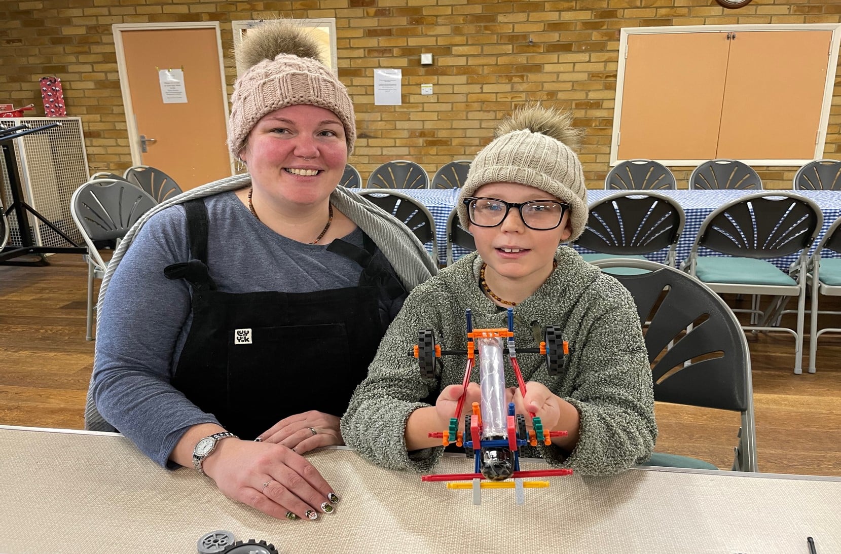 A woman and boy sit together at a table proudly looking at a car they have created together